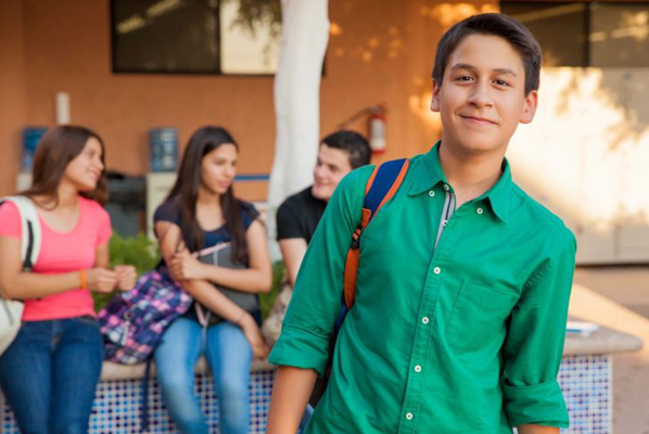 A boy in green shirt and blue jeans standing next to other people.